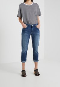 Harmaavalkoraidallinen T-paita, siniset farkkukorkeavyötäröiset lyhytlahkeiset farkut, joissa käännetyt lahkeet, ja mustat avokkaat, joissa on hapsukoristeet.