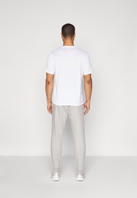 Hvid t-shirt med korte ærmer og grå sweatpants. Outfitet er afslappet med en løs pasform. Sweatpantsene har elastiske manchetter og lommer.