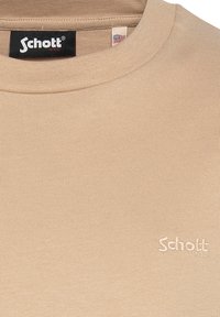 Maglietta a righe beige con scollatura rotonda. Presenta un piccolo logo ricamato bianco sul petto. Tessuto morbido, vestibilità casual.