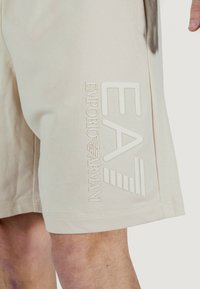 Shorts beige realizzati in tessuto morbido, con un grande logo in rilievo e testo sul lato. Il design presenta cuciture pulite e una vestibilità dritta.