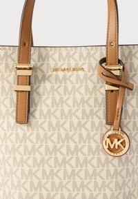Beige håndtaske med et struktureret design, kontrasterende brune læderstropper, hardware i guldfarve og et cirkulært MK-logo som accent.