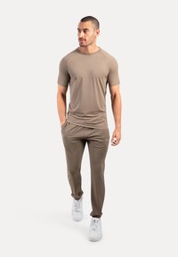 Camisa deportiva beige de manga corta combinada con pantalones beige ajustados y zapatillas blancas. Tejido suave, diseño simple, sin patrones ni acentos visibles.