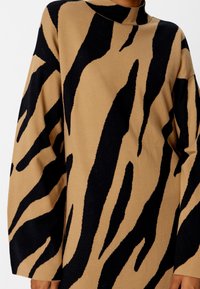 Maglione lavorato a maglia con una base beige e audaci motivi a strisce di tigre neri, colletto alto e maniche oversize per un fit comodo.