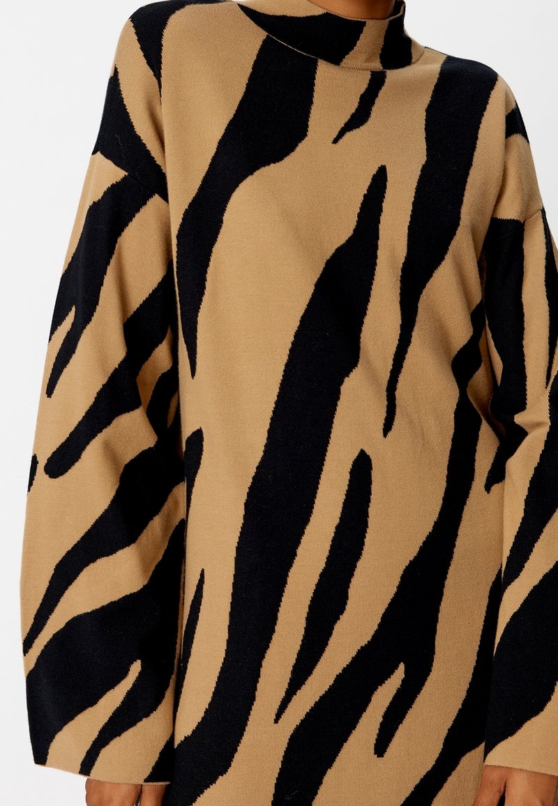 Strickpullover mit einem sandfarbenen Grundton und auffälligen schwarzen Tigerstreifenmustern, hohem Kragen und übergroßen Ärmeln für einen lockeren Sitz.