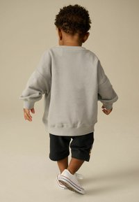 Sweatshirt gris clair à épaules tombantes, shorts noirs et baskets blanches. Design simple, texture douce et coupe décontractée.