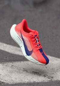 Běžecká obuv Nike ZoomX s živou korálovou svrškem s texturou z prodyšné síťoviny, fialovými akcenty a bílou polstrovanou podrážkou.