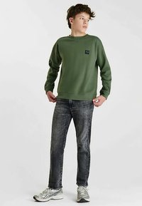 Groene sweatshirt met ronde hals en een klein logoplaatje, gecombineerd met donkergrijze jeans en zilveren sneakers. Soepele textuur, casual pasvorm.