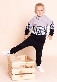 Szara bluza z kapturem z czarnymi i białymi, wzorzystymi rękawami, zestawiona z czarnymi joggerami i białymi butami, stojąca na drewnianej skrzyni.