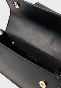 Interior de uma bolsa de couro preto com um compartimento com zíper e fecho magnético. Textura suave com detalhes em metal dourado.