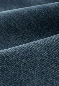Denim fabric in dark blue with a textured surface. The material has a subtle weave pattern, with varying shades creating depth.