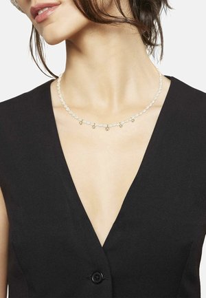 Collar de perlas con acentos dorados, que presenta pequeñas cuentas redondeadas de oro y perlas de diferentes tamaños, llevado sobre una prenda negra de escote en V.