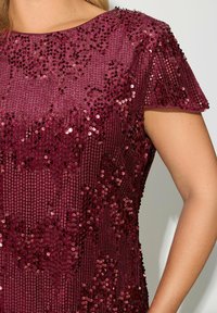 Burgunderfärgad paljettopp med rund halsringning och korta ärmar. Har en texturerad yta med glittrande runda paljetter i varierande storlekar.