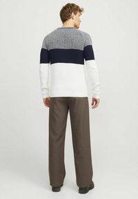 Pulover tricotat în gri, albastru marin și alb, cu design în blocuri de culoare; textură ribbată; decolteu rotund; asortat cu pantaloni căprui și pantofi negri.