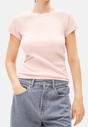 Femme portant un haut côtelé à manches courtes rose pâle rentré dans un jean en denim bleu taille haute, une main dans la poche.