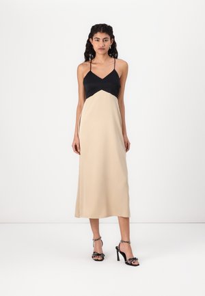 Abito maxi nero e beige con spalline sottili, design a pannello triangolare sul corpetto e tessuto dalla texture liscia. Sandali neri con tacco alto.