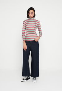 Helancă cu dungi în verde, roșu și roz; pantaloni evazați din denim închis; teniși Converse negri și albi; ochelari de soare mov.