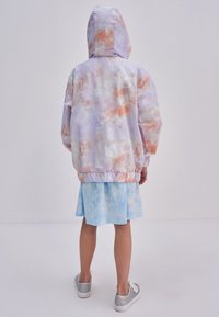 Leichte, pastellfarbene Jacke mit Kapuze, die ein wolkenähnliches Muster in Lavendel und Pfirsich aufweist. Elastischer Bund, lässige Passform.