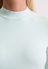 Hellblaues, geripptes Rollkragenoberteil mit taillierter Silhouette. Sanfte Textur und nahtlose Kanten am Kragen, die ein minimalistisches Design zur Schau stellen.