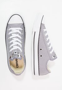 Baskets en toile grise texturée avec des lacets blancs, dotées d'une semelle en caoutchouc, d'une bande noire et d'un design en mesh pour la respirabilité.