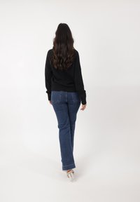 Czarny sweter z długimi rękawami w połączeniu z niebieskimi dzwonami. Przezroczyste, na obcasie buty. Włosy falowane, pozostawione luźno. Widok z tyłu.