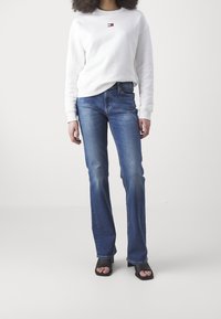 Felpa bianca con un piccolo logo, abbinata a jeans blu con design a gamba dritta e sfumature sottili. Sandali neri con tacco a blocco.