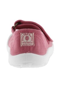 Zapato de lona rosa con suela blanca, que presenta una correa trasera y una etiqueta que muestra "Victoria Barefoot". Diseño simple y ligero.