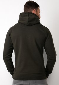 Felpa verde scurorealizzata in morbido tessuto, con un cappuccio alto, maniche aderenti e polsini a costine. Texture liscia senza loghi visibili.