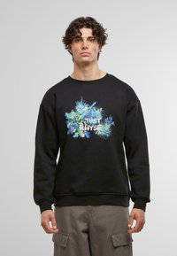 Svart hettegenser med et fargerikt blomsterdesign i midten, der teksten "JUST RHYSE" står. Laget av en bomullsblanding med ribbestrikkede mansjetter.