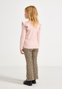 Light pink long-sleeve top with ruffle accents on shoulders, paired with beige leopard-print flared pants and black chunky shoes.