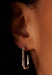 Silberne Ohrringe mit einem geschwungenen Design, das eine Reihe von kleinen, klaren Edelsteinen entlang der geschwungenen Kante und eine glatte metallische Oberfläche aufweist.