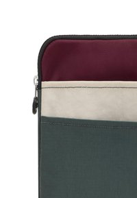Une pochette zippée en tissu vert foncé présente une doublure bordeaux et une bande accent blanche. La surface texturée et les détails de couture robustes sont visibles.