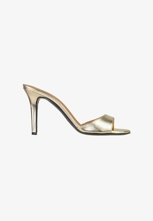 Mule metallizzato oro open-toe con tacco alto sottile e una fascia larga sul piede, mostrato di profilo su sfondo bianco.