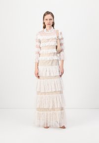 Rochie din dantelă cu volane stratificate, având un top transparent, mâneci lungi și un corset ajustat în tonuri de alb și nud. Include o geantă ușoară.