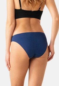 Sous-vêtements hipster en coton bleu marine avec une texture lisse, couture arrière courbée et design taille mi-haute. Les bretelles de soutien-gorge noires sont visibles au-dessus.