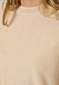 Beige džemperis ar ribotu apaļu kakla izgriezumu, izgatavots no smalka teksturēta dziju auduma. Viegls un mīksts, ar gludu virsmu.