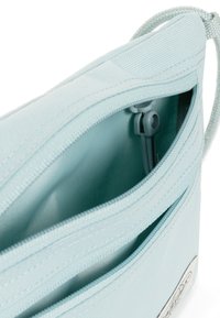 Borsa azzurra chiusa con cerniera, con un esterno liscio e texture. L'interno presenta una tasca con una cerniera coordinata dello stesso colore.