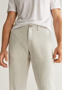 Lichtgrijze linnen broek met een relaxte pasvorm, voorzien van een knoopsluiting en zijzakken. De stof heeft een soepele textuur en een subtiele glans.