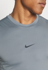 Graues Sportshirt aus glattem, dehnbarem Material mit einem Rundhalsausschnitt und schwarzem Nike-Logo auf der Brust. Verfügt über flache Nähte.