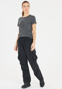 Grå kortärmad t-shirt med tryckt mönster; svarta cargo-byxor med flera fickor och avslappnad passform; svarta snörkängor.