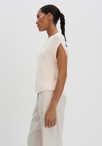 Top lavorato a maglia rosa chiaro con maniche a cappuccio e vestibilità comoda, abbinato a pantaloni beige. Texture morbida, design minimalista e spacchi laterali.