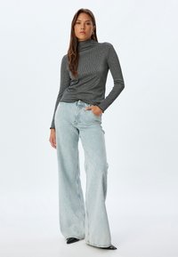 Grauer gerippter Rollkragenpullover kombiniert mit hellblauen weit geschnittenen Jeans mit einem Diamantmuster und schwarzen spitzen Absätzen.