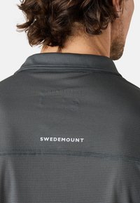 Grå kortärmad skjorta med ett strukturerat mönster. Har en krage och ordet "SWEDEMOUNT" tryckt i vitt på baksidan.