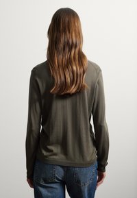 Camiseta de manga larga en color verde oliva, hecha de una tela suave, con escote redondeado y un corte holgado, combinada con jeans azules desgastados.