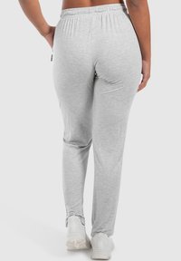 Graue Baumwoll-Jogginghosen mit elastischem Bund, seitlichen Taschen und Knöchelverzierungen, kombiniert mit weißen Sportschuhen.