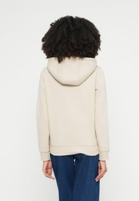 Μπεζ φούτερ με μαλακό ύφασμα, με μεγάλο κουκούλα, τσέπη καγκουρό και ριμπ μανσέτες. Συνδυασμένο με φαρδιά μπλε τζιν.