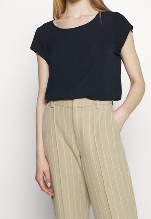 Haut bleu marine à manches courtes avec un col rond, associé à un pantalon beige à rayures verticales, coupe ajustée et poches latérales.