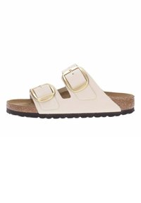 Light beige two-strap sandal with gold buckles, cork footbed, and black rubber outsole. Smooth leather material with open design.