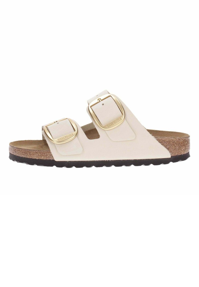 Light beige two-strap sandal with gold buckles, cork footbed, and black rubber outsole. Smooth leather material with open design.