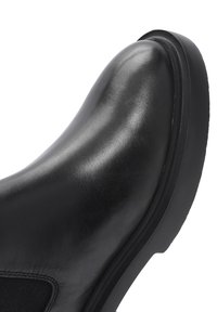 Botín Chelsea de cuero negro liso con punta redondeada y suela gruesa, con panel lateral elástico para poner y quitar fácilmente.