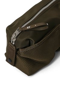 Mørk olivengrøn taske med lynlås, der har et mesh-sidenpanel, robust stof og en stoftrækflap med trykt tekst.